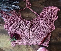 a pink crocheted top with a flower on it and yarn next to it