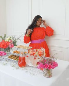 a woman standing in front of a table filled with desserts and flowers on it