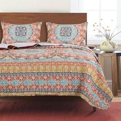 a bed covered in a colorful quilt next to a night stand with flowers on it