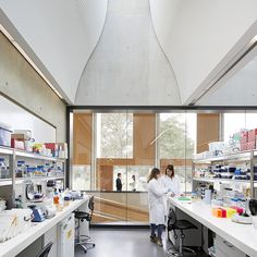 two women in white lab coats are standing by the counter and looking at items on shelves