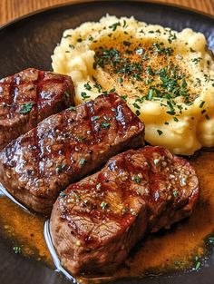 steak, mashed potatoes and gravy on a black plate with green garnish