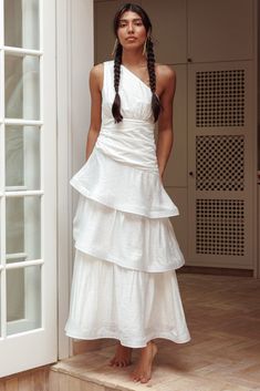 a woman standing in front of a door wearing a white dress with tiered layers