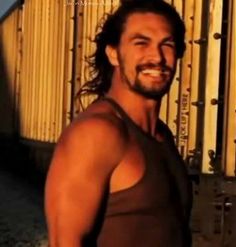 a man with long hair and beard standing in front of a fence smiling at the camera