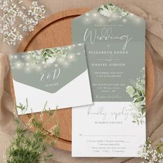 the wedding stationery is set on top of a wooden platter with flowers and greenery