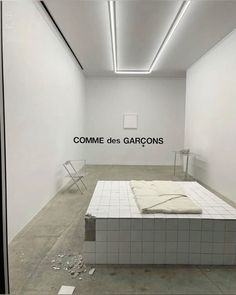 an empty room with a bed in it and the words comme des garcons on the wall