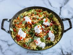 a pan filled with pasta and vegetables on top of a marble counter