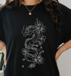 Be a trend-setter in our River Dragon Tee! Flaunt your bad-ass attitude with the cool dragon print, while still maintaining comfort with the 100% cotton, relaxed fit. You're no princess, you're a dragon ready to take on the streets. 🐉 Ain't no one gonna stop you! This is a unisex tee so check the size guide for measurements! and if you want to rock that oversized look go up a few sizes. This product is made especially for you as soon as you place an order, which is why it takes us a bit longer Dragon Graphic Tee, Cotton T-shirt With Dragon Print, Black Crew Neck T-shirt With Dragon Print, Black Cotton Tops With Dragon Print, Black Cotton Top With Dragon Print, Short Sleeve Tops With Dragon Print For Streetwear, Casual Crew Neck T-shirt With Dragon Print, Dragon Print Crew Neck Top For Streetwear, Casual Dragon Design Tops For Streetwear