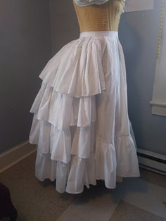 This listing is for a made to order ruffled petticoat and is made from a high quality cotton - here it is shown over a wire bustle (not included) but can be worn without one (is about 3 inches longer in the back). It closes on the left hand side with a button, One ruffle goes around the entire bottom, and additional ruffles on the back. I will need to know your waist measurement and the length of the petticoat (waist to where you want the petticoat to end). Please allow 3-4 weeks for the making of this item as it is made to order. If you have any custom requests please contact me with more details of what you're looking for - I am happy to work to your specifications!  Different fabrics & patterns available upon request (please note that a change in fabric may alter the total price of this Tiered Ruffled Petticoat, Costume Petticoat With Tiered Skirt, Full Skirt With Ruffles In Crinoline, Fitted Full Petticoat With Ruffled Skirt, Full Crinoline Skirt With Ruffles, Can-can Crinoline Petticoat With Tiered Skirt, Can-can Crinoline Tiered Petticoat, Voluminous Ruffled Crinoline Petticoat, White Costume Skirt With Attached Cancan