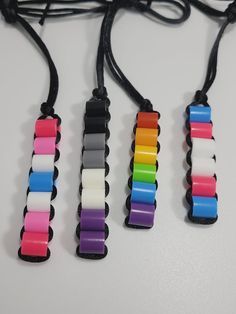 four different colored bracelets are hanging from a string on a white surface with black cords