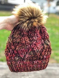 a hand holding a knitted hat with a pom - pom