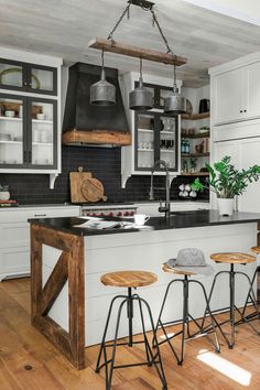 a kitchen with white cabinets and wooden stools in front of an island that has black counter tops