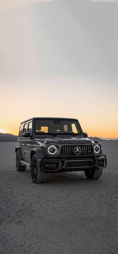 a mercedes g - class is parked in the desert at sunset with its lights on