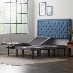 an adjustable bed frame in front of a blue upholstered headboard on a hardwood floor