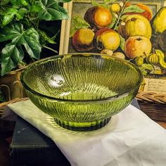 a green glass bowl sitting on top of a table next to a basket filled with fruit