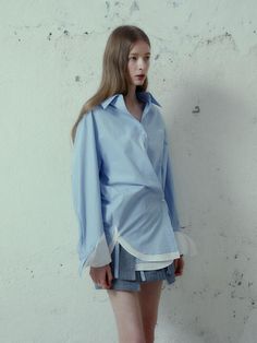 This product is a creative take on the classic button-up shirt, featuring double-layered cuffs that give it a unique and avant-garde appearance. The relaxed fit ensures a comfortable drape over the body, while the detail-oriented design speaks to a modern, fashion-forward aesthetic. The ensemble is complemented by a pair of tailored shorts that balance the shirt's volume and add to the contemporary styling of the set. - The shirt's double-layered cuffs create a distinctive style statement, setting it apart from traditional designs.- A relaxed fit allows for effortless pairing with various bottoms, ensuring versatility in styling options.- Tailored shorts provide a structured contrast to the shirt's loose form, resulting in a balanced and polished outfit.- Constructed with a focus on q Spring Button-up Shirt For Layering, Chic Cotton Shirt For Layering, Blue Button-up Shirt For Layering, Blue Long Sleeve Shirt With Cuffed Sleeves, Spring Shirt With Button Cuffs For Layering, Spring Layering Shirt With Collar, Spring Layering Shirt With Button Cuffs, Spring Tops With Striped Cuffs And Relaxed Fit, Blue Tops With Cuffed Sleeves For Fall