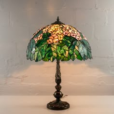 a stained glass lamp on a table next to a white brick wall and flooring