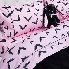 a stuffed animal sitting on top of a bed covered in pink and black bat sheets