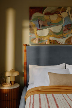 a bed with white sheets and pillows next to a painting