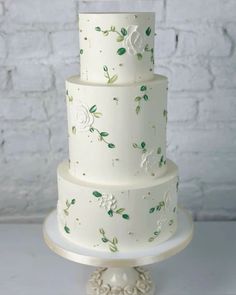 a three tiered white cake with green leaves and flowers on it's side