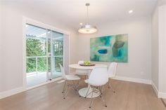 a dining room table with white chairs and a painting on the wall in front of it