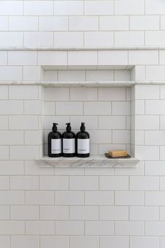 three bottles are sitting on a shelf in the bathroom, one is black and white