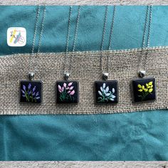 four square pendants with flowers painted on them sitting on a piece of burlock