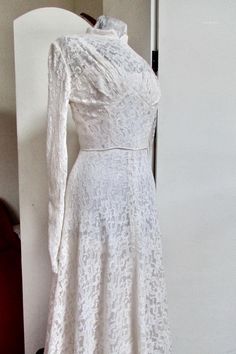 a white dress is displayed on a mannequin headdress with an open collar and long sleeves