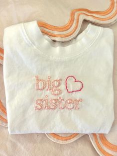 Celebrate your growing family with this lovely Big Sister shirt! With two tones of double-stitched pink thread and a precious heart, your daughter will be able to show all her love for the new baby. Pink Embroidered Cotton T-shirt, Cute Pink T-shirt With Letter Embroidery, Pink Short Sleeve T-shirt With Machine Embroidery, White T-shirt With Letter Embroidery As Gift, Spring Pink T-shirt With Custom Embroidery, Pink Cotton Top With Machine Embroidery, Cute Pink Tops For Family Occasions, White T-shirt With Letter Embroidery For Gift, Cute White T-shirt With Machine Embroidery