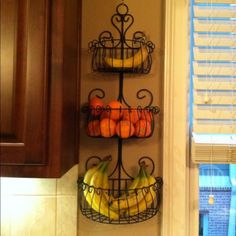 two metal baskets filled with fruit on top of a kitchen counter next to a window