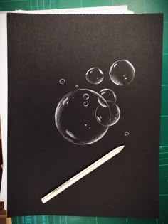 a drawing of soap bubbles on black paper with a white pencil next to it and green background