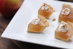 four pieces of dessert on a plate with an apple in the background