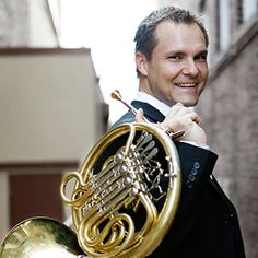 a man in a tuxedo is holding a french horn