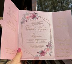 a person holding up a pink and gold wedding card with flowers on the inside of it