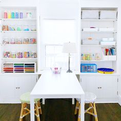 a white table and two stools in a room with bookshelves on the wall