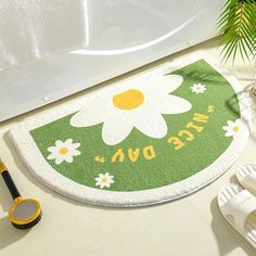 a green and white door mat with a flower on it next to some sandals, sand and a potted plant