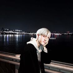 a young man standing on top of a boat near the ocean at night with city lights in the background