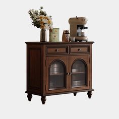 a wooden cabinet with glass doors and flowers on top, next to an espresso machine