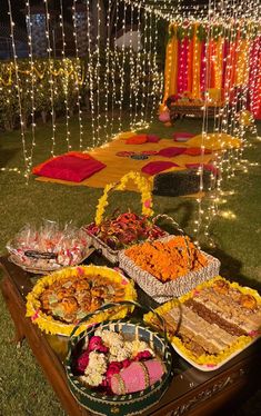 a table topped with lots of food on top of a lush green field covered in lights