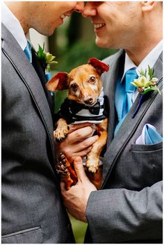 two men in suits are holding a small dog