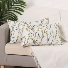 two decorative pillows on a couch next to a potted plant and a white blanket