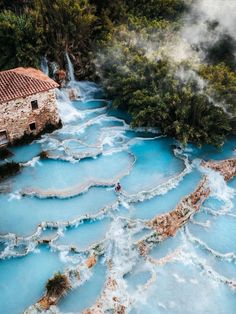 a man standing in the middle of a blue pool surrounded by trees and water with steam rising from it