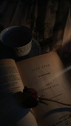 an open book with a single rose on it next to a cup and saucer