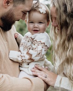 a man and woman holding a baby in their arms while they smile at each other