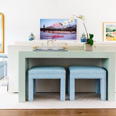 two blue stools sitting under a table in front of a painting on the wall