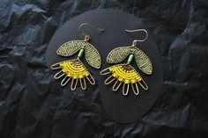 a pair of yellow and green earrings sitting on top of a black piece of paper