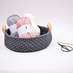 yarn and scissors are in a basket next to some crochet hooks on a white background