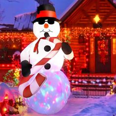 a snowman with a candy cane standing in front of a house decorated for christmas