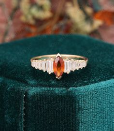 an orange stone ring sitting on top of a green velvet covered cushioned box with flowers in the background