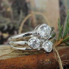 three diamond rings sitting on top of a piece of wood next to an evergreen branch