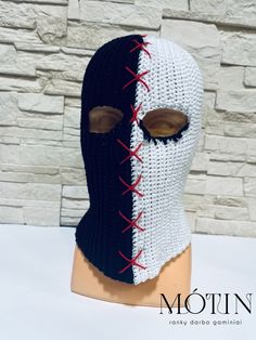 a crocheted mask with red and white stitches on the side, sitting on top of a mannequin head